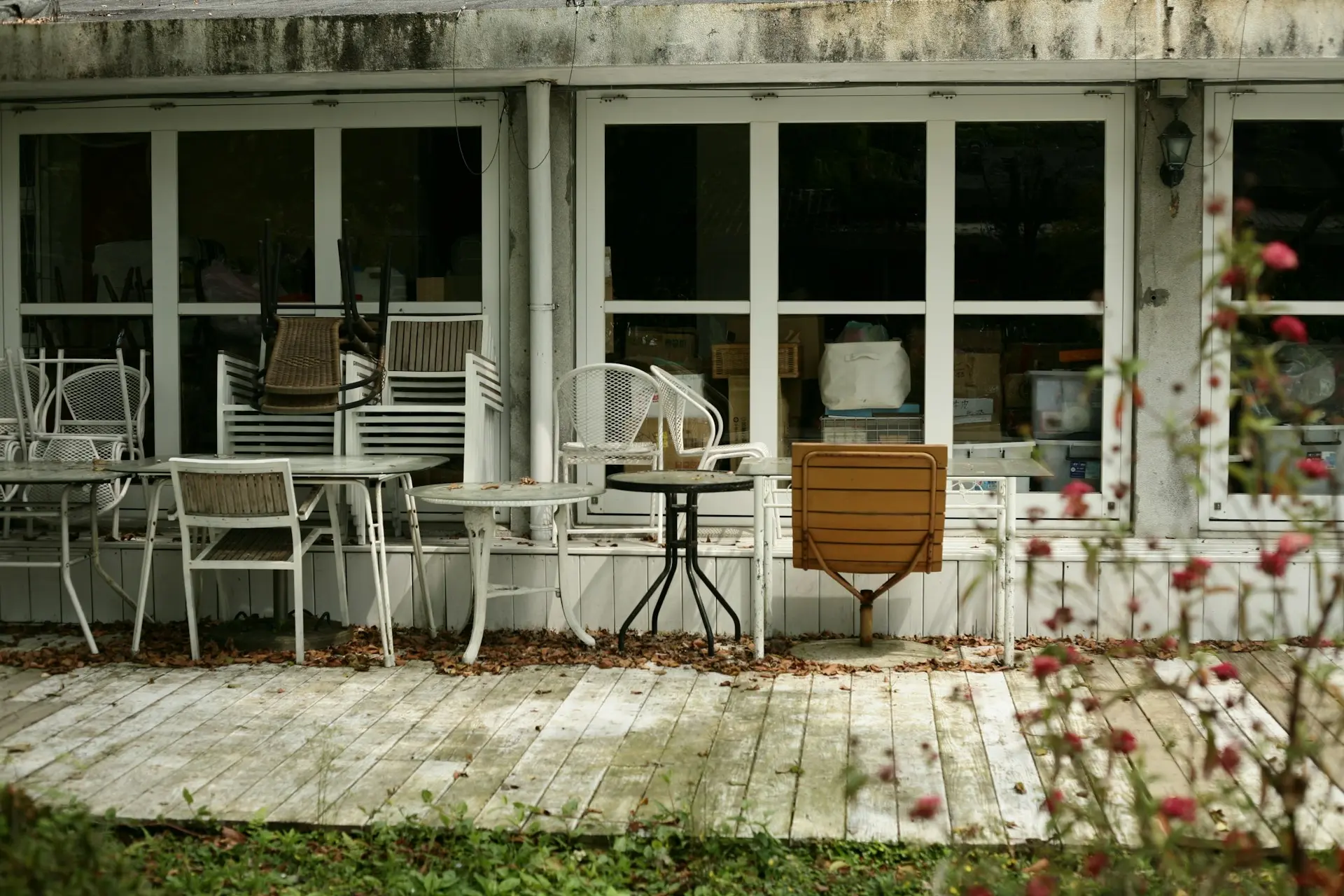 Une terrasse mal entretenue, des feuilles mortes sur un plancher sale, des tables et des chaises en mauvais état empilées devant des fenêtres sales qui donnent sur le restaurant.